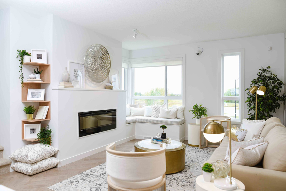 Living area with beige couch and modern classy gold accent decor, window reading nook with white pillows and large windows. Cobalt Beach Showhome in Jensen Lakes St. Albert