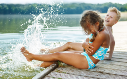 Two kids splashing by lake, boy and girl on dock playing by the water.