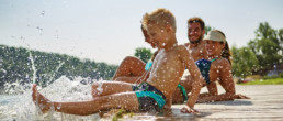 Happy family at a lake having fun and splashing water in summer.