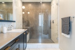 Bathroom shower with glass doors and grey stone, paired with white marble floor. Showhome in Jensen Lakes.