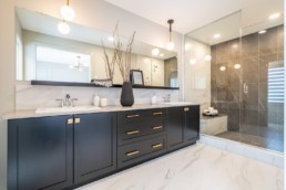 Double sink bathroom with black and gold cabinets. Glass lined shower with marble floors in Pacesetter Calypso showhome in Jensen Lakes St. Albert