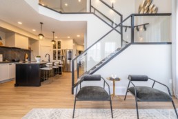 Main floor area with black railing staircase, gold accented kitchen with white walls and modern design. In Jensen Lakes showhomes. The Calypso by Pacesetter homes in St. Albert.