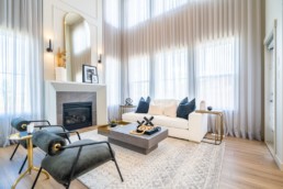 Great room with ceiling high windows and stone lines fireplace. Gold and grey accent decor with white furniture. In Pacesetter homes Calypso showhome in St. Albert's Lakeside living community of Jensen Lakes.
