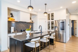 The Calypso showhome by Pacesetter homes in Jensen Lakes St. Albert. Kitchen with grey and white countertops modern gold and white design and accent wine wall.